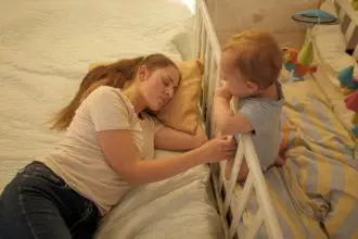 Tired exhausted mother rocking baby bed and sleeping. Concept of parenting, parent fatigue and