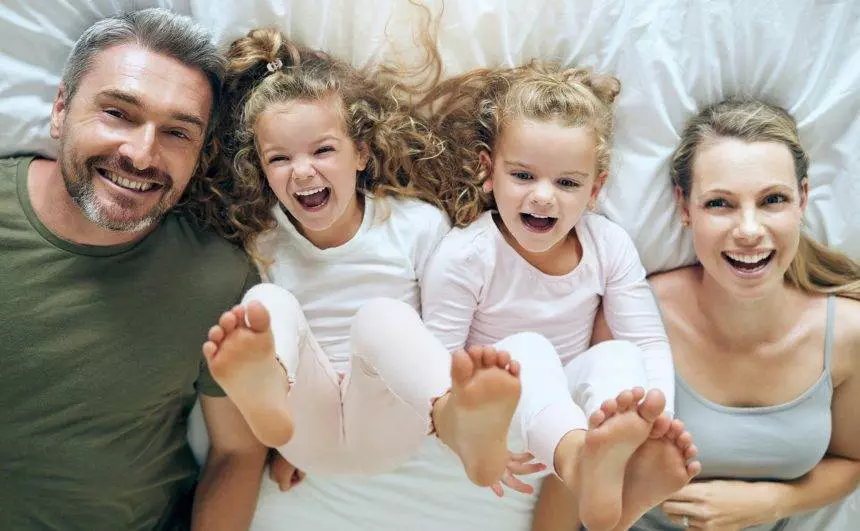Top view, happy and family with twins in bed smiling together with parents in the morning at home o